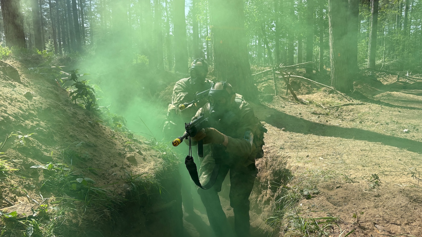 Två Ukrainska soldater som övar skyttegravskrig med skyddsmasker på. De kommer ut ur grön rök. 